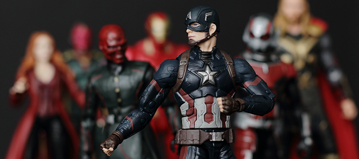 An action figure of Caption American stands front and center, posed with his fists clenched and ready to fight. Behind him and slightly out of focus, stand other action figures from the Marvel Universe
