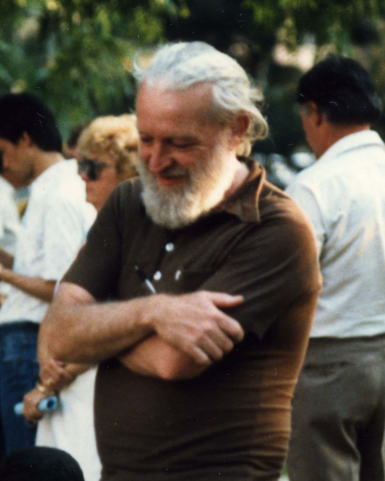 An image of C. Loring Brace: a tall white man with gray hair and beard, wearing a black t-shirt and standing with his arms crossed.